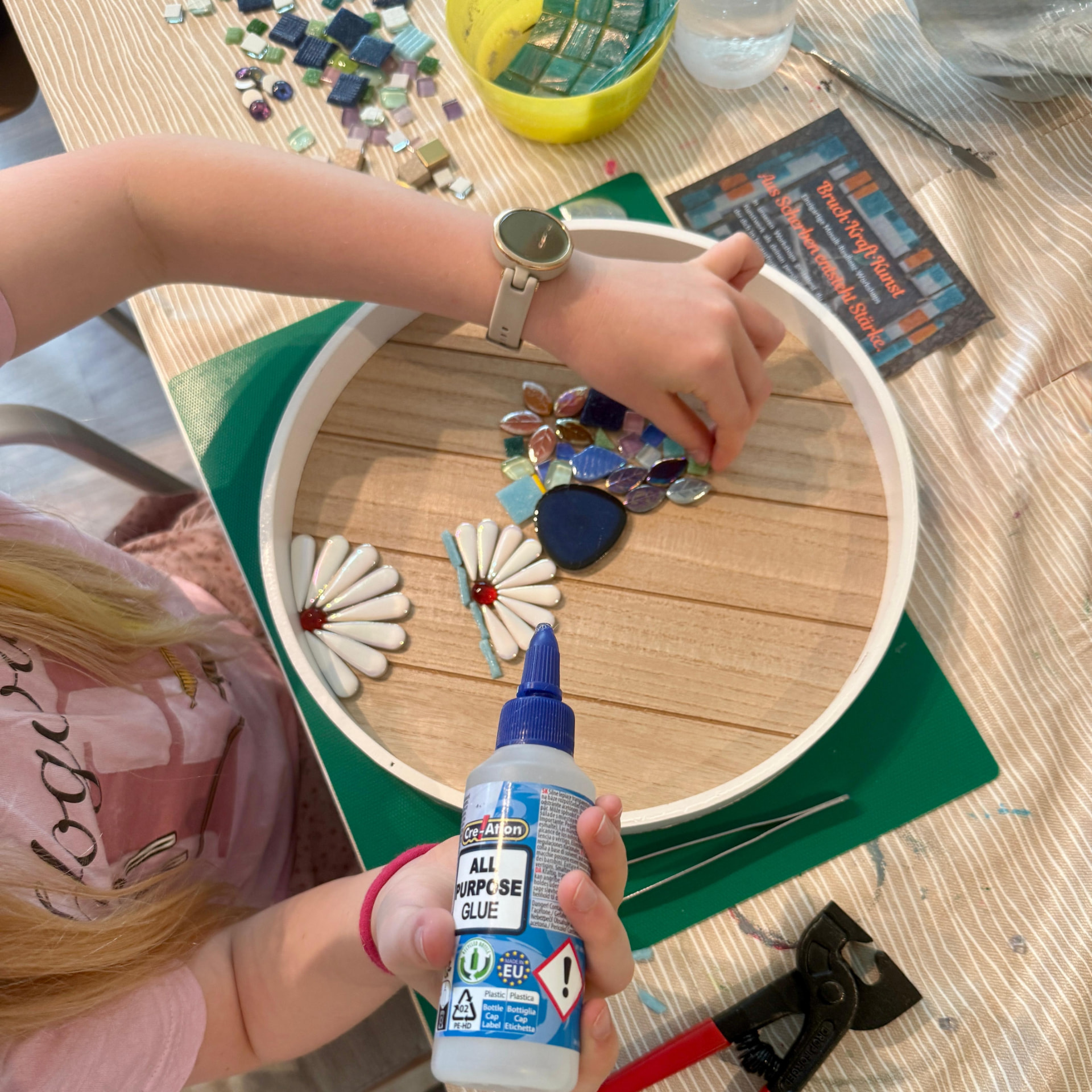 Kind gestaltet ein rundes Mosaiktablett mit Gänseblümchen-Motiven aus Glassteinen